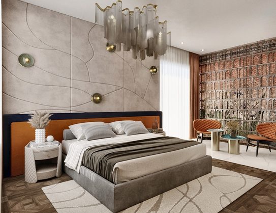 A bed with a rust leather headboard against a sculpted plaster wall hung with brass spheres, under a glass chandelier.