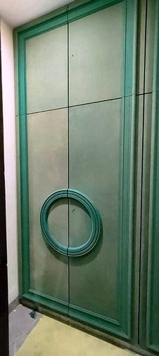 A tall green fluted door with a circular ring detail set into it, standing finished in an unfinished room.