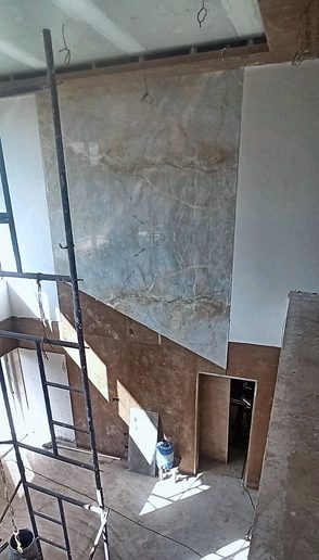 The double-height living wall under construction — the first stone slab set, a ladder against it, the floor still bare.