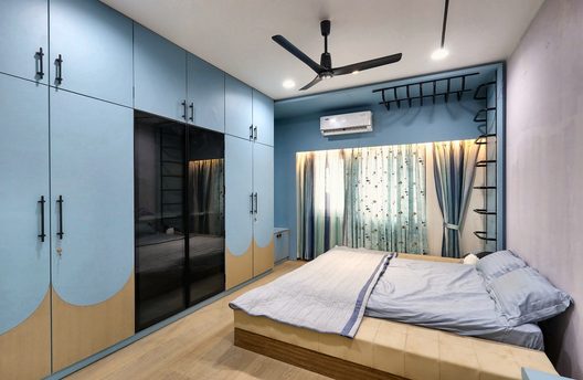 The bedroom built — the same pale blue wardrobes with the same scalloped base, and the bed against the far wall.
