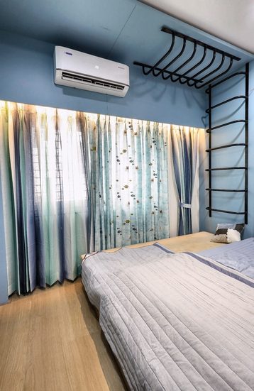 A bedroom with a deep blue wall, patterned sheer curtains and a bed against the window.