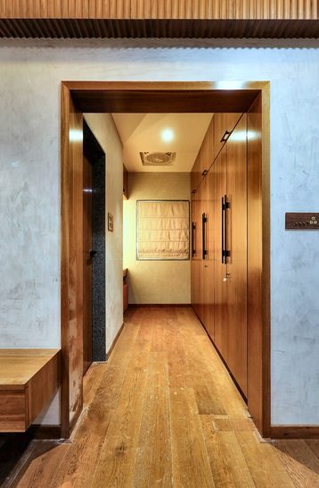 A corridor with a timber floor, looking through a teak-lined door frame into the room beyond.
