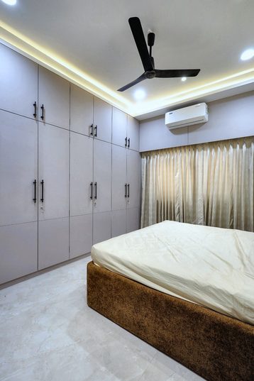 A bedroom lined on one side with white gloss wardrobes, the bed on a timber base.